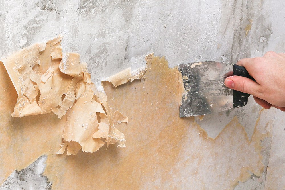 Persoon gebruikt een plamuurmes om behang van gipsplaten te verwijderen.