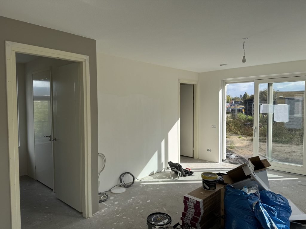 Woonkamer tijdens de afwerking, met materiaal en verfemmers op de vloer