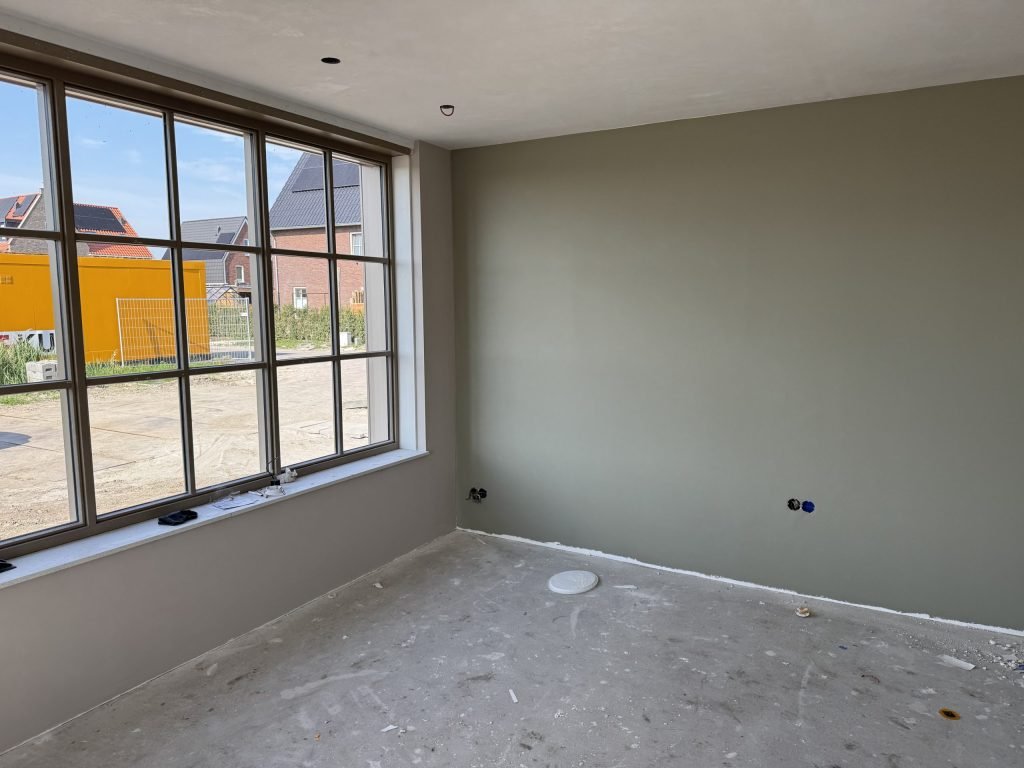 Kamer met een egaal gesausde wand in een grijsgroene tint en een groot raam