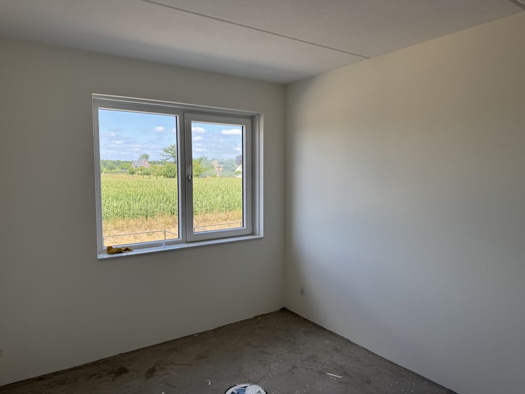 Lege kamer met gladde, lichte wanden en een raam, klaar voor de afwerking