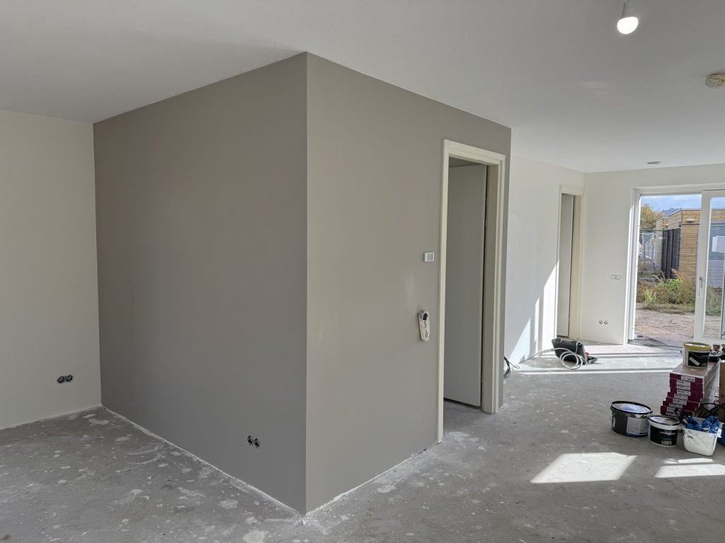 Pas afgewerkte grijze wand in een nieuwbouwwoning, met verfemmers op de vloer