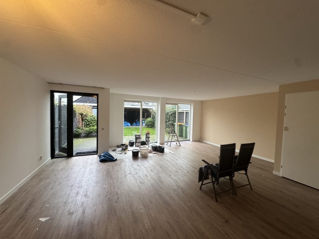 Ruime woonkamer met lichte, gesausde wanden en een houten vloer
