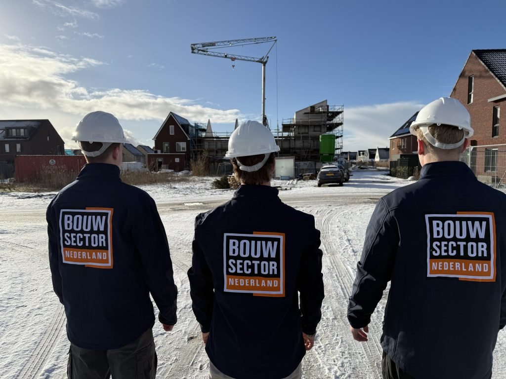 Drie vakmensen van Bouwsector Nederland in werkjassen met logo op een besneeuwde bouwplaats